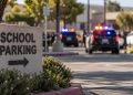 Close-up of a school parking sign with blurred police activity in the background after a student battery in Ventura.