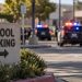 Close-up of a school parking sign with blurred police activity in the background after a student battery in Ventura.