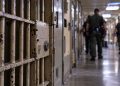 Close-up of a secured California prison corridor with a barred cell door and blurred correctional officers in the background, illustrating a homicide investigation inside Pelican Bay State Prison.