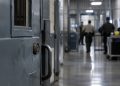 Close-up of a secured prison corridor with a metal door and blurred correctional staff activity in the background, illustrating an alleged attack on a prison counselor in Lancaster.