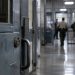 Close-up of a secured prison corridor with a metal door and blurred correctional staff activity in the background, illustrating an alleged attack on a prison counselor in Lancaster.