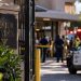 Close-up of a senior living facility entrance with blurred police vehicles and emergency responders outside after a workplace shooting in South Los Angeles.