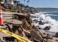 Close-up of a sun-baked Southern California coastline with large waves and damaged shoreline structures in the background, illustrating extreme heat and coastal recovery.