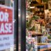 Close-up of a toy and book store window displaying dinosaur toys, children's books and stuffed animals, with a blurred “FOR LEASE” sign in the foreground.