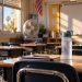 Close-up of an empty classroom with a water bottle, portable fan and desks in warm sunlight, illustrating heat challenges at Southern California schools.