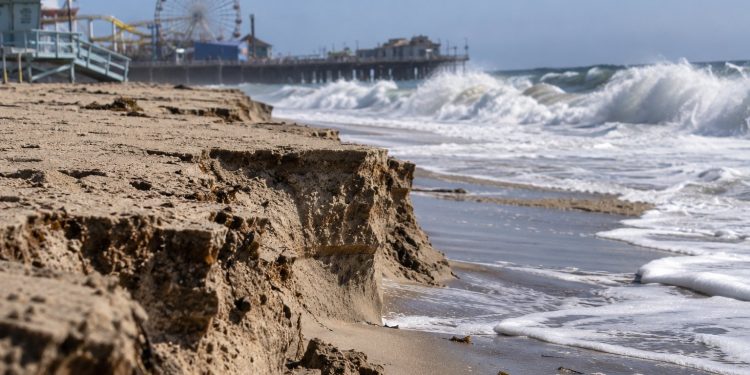Close-up of an eroded Santa Monica beach with exposed sand layers and large waves, illustrating the coastal damage that forced Ocean Way Festival to be canceled.