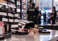 Close-up of beauty products and shopping bags on a retail store counter, with blurred police activity and store shelves in the background, illustrating a Southern California theft investigation.