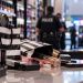 Close-up of beauty products and shopping bags on a retail store counter, with blurred police activity and store shelves in the background, illustrating a Southern California theft investigation.