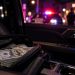 Close-up of cash and a vehicle interior at night with blurred emergency lights in the background, illustrating an armed robbery targeting a restaurant investor in Alhambra.