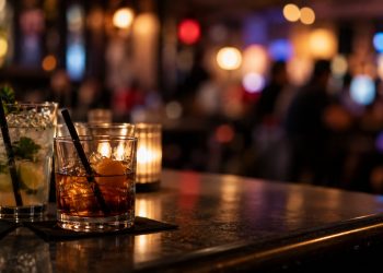 Close-up of cocktails on a bar counter with a heavily blurred nightlife background, illustrating the closure of a longtime West Hollywood bar and restaurant.