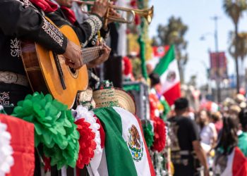 Close-up of colorful Mexican Independence Day parade decorations, mariachi instruments and festive flags along a crowded East Los Angeles street.