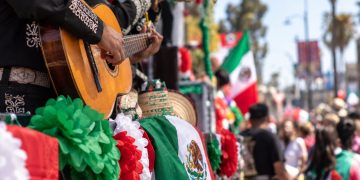Close-up of colorful Mexican Independence Day parade decorations, mariachi instruments and festive flags along a crowded East Los Angeles street.
