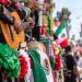 Close-up of colorful Mexican Independence Day parade decorations, mariachi instruments and festive flags along a crowded East Los Angeles street.