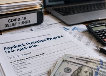 Close-up of federal loan documents and a laptop beside a calculator and financial records, illustrating a COVID-19 business-relief fraud investigation.