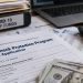 Close-up of federal loan documents and a laptop beside a calculator and financial records, illustrating a COVID-19 business-relief fraud investigation.