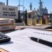 Close-up of military contracting documents and a calculator on a desk, with a blurred Navy facility in the background, illustrating a federal fraud case.