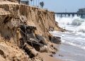 Close-up of severe beach erosion at Newport Beach, with a steep sand drop-off, exposed debris and large waves along the shoreline.