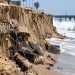Close-up of severe beach erosion at Newport Beach, with a steep sand drop-off, exposed debris and large waves along the shoreline.