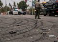 Close-up of tire marks and scattered debris across an intersection, with a blurred deputy and impounded vehicle visible in the background.