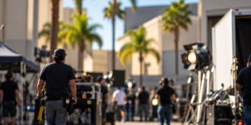Film production crew working around lighting equipment and equipment carts on a studio backlot, illustrating Hollywood workforce concerns tied to a major merger.