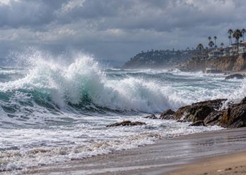 Large waves breaking along a Southern California beach under cloudy skies, illustrating powerful swells from Hurricanes Polo and Odalys.