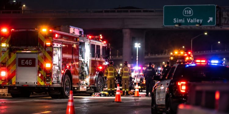 Nighttime emergency response on a Simi Valley freeway, with a fire engine, police vehicle, firefighters and traffic cones beneath an overpass.