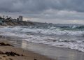 Southern California beach with choppy ocean surf, wet sand and heavy overcast skies, illustrating coastal impacts expected from Hurricane Polo.