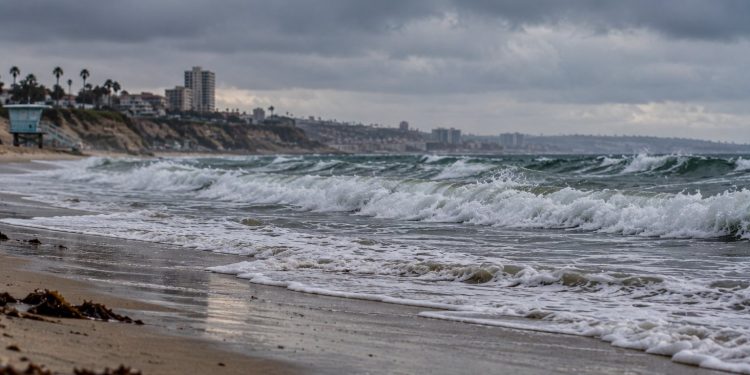 Southern California beach with choppy ocean surf, wet sand and heavy overcast skies, illustrating coastal impacts expected from Hurricane Polo.
