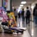 Close-up of assorted colorful drug packages and vaping devices on a table, with a heavily blurred school hallway and students in the background, illustrating an alleged narcotics operation targeting young students in Ventura County.
