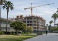 A concrete-framed building under construction beside older classroom buildings on a Los Angeles community college campus in afternoon daylight.