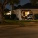 A one-story stucco house on a residential street in Sherman Oaks with a damaged exterior wall, seen from across the street at night under street lamps.