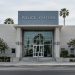 A police station building in Van Nuys in neutral daylight, its institutional facade sharp and centered, palm trees and neighborhood buildings blurred behind.