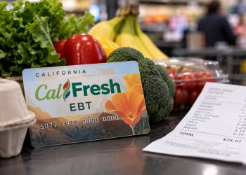 Close-up of a CalFresh EBT card beside fresh groceries and a supermarket receipt, illustrating changes to food assistance benefits in California.