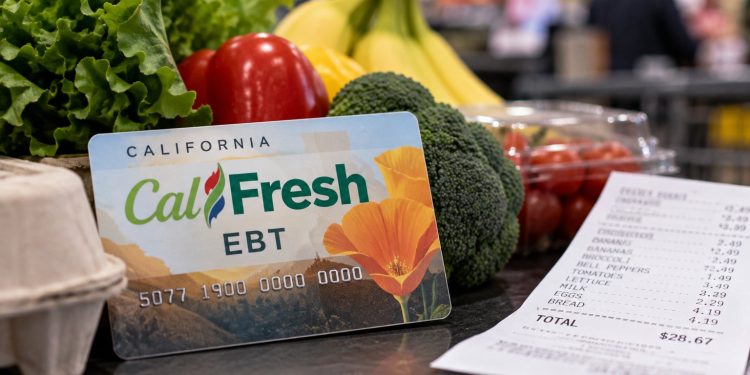Close-up of a CalFresh EBT card beside fresh groceries and a supermarket receipt, illustrating changes to food assistance benefits in California.
