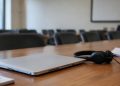Close-up of a closed laptop, a headset and papers with illegible text on a conference table, illustrating the Los Angeles homeless services meeting.