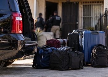 Close-up of a dark vehicle and stacked travel bags near a Los Angeles residential property, illustrating a large-scale human smuggling investigation.