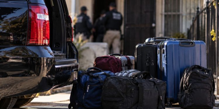 Close-up of a dark vehicle and stacked travel bags near a Los Angeles residential property, illustrating a large-scale human smuggling investigation.