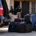 Close-up of a dark vehicle and stacked travel bags near a Los Angeles residential property, illustrating a large-scale human smuggling investigation.