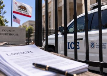 Close-up of a federal immigration enforcement vehicle behind a courthouse fence, with blurred California flags and legal documents in the foreground.