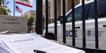 Close-up of a federal immigration enforcement vehicle behind a courthouse fence, with blurred California flags and legal documents in the foreground.