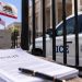 Close-up of a federal immigration enforcement vehicle behind a courthouse fence, with blurred California flags and legal documents in the foreground.