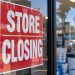Close-up of a red “STORE CLOSING” sign taped to a retail storefront window, with pool supply products and the parking lot softly blurred in the background.