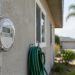 Close-up of a residential electric meter on a stucco wall of a single-story Los Angeles home, with a garden hose and palm tree softly blurred behind.