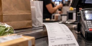 Close-up of a retail checkout counter with shopping bags and a sales receipt, illustrating the Los Angeles County sales tax increase taking effect Oct. 1.