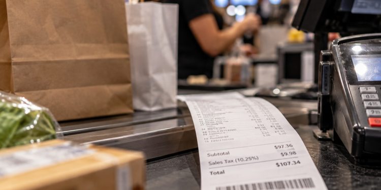 Close-up of a retail checkout counter with shopping bags and a sales receipt, illustrating the Los Angeles County sales tax increase taking effect Oct. 1.