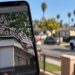 Close-up of a smartphone displaying a digitally generated image of a Gaboon viper, with a blurred Santa Ana residential neighborhood in the background.