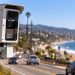 Close-up of a speed enforcement camera along Pacific Coast Highway in Malibu, with the roadway and California coastline blurred in the background.