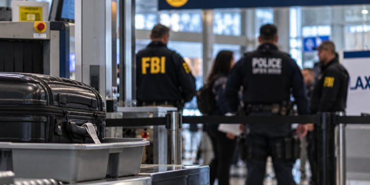 Close-up of an airport security checkpoint and blurred federal agents near an international departure gate, illustrating an alleged foreign-agent investigation at LAX.