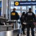 Close-up of an airport security checkpoint and blurred federal agents near an international departure gate, illustrating an alleged foreign-agent investigation at LAX.