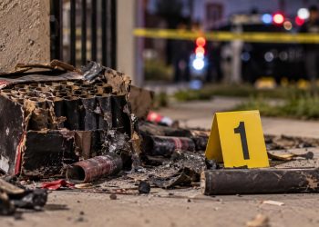 Close-up of damaged pyrotechnic materials and an evidence marker near a residential scene, illustrating an investigation into a fatal South Los Angeles explosion.